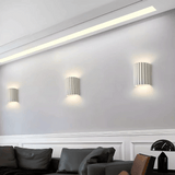 Modern wall lights on a white wall with a sofa and decorative items in the foreground.