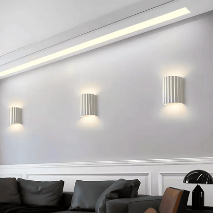 Modern wall lights on a white wall with a sofa and decorative items in the foreground.