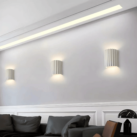 Modern wall lights on a white wall with a sofa and decorative items in the foreground.