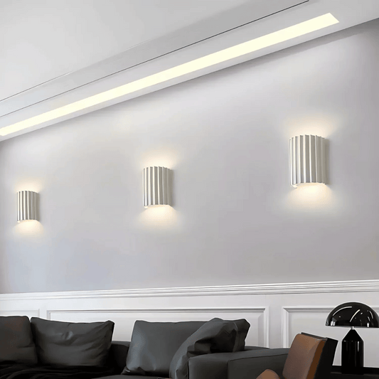 Modern wall lights on a white wall with a sofa and decorative items in the foreground.