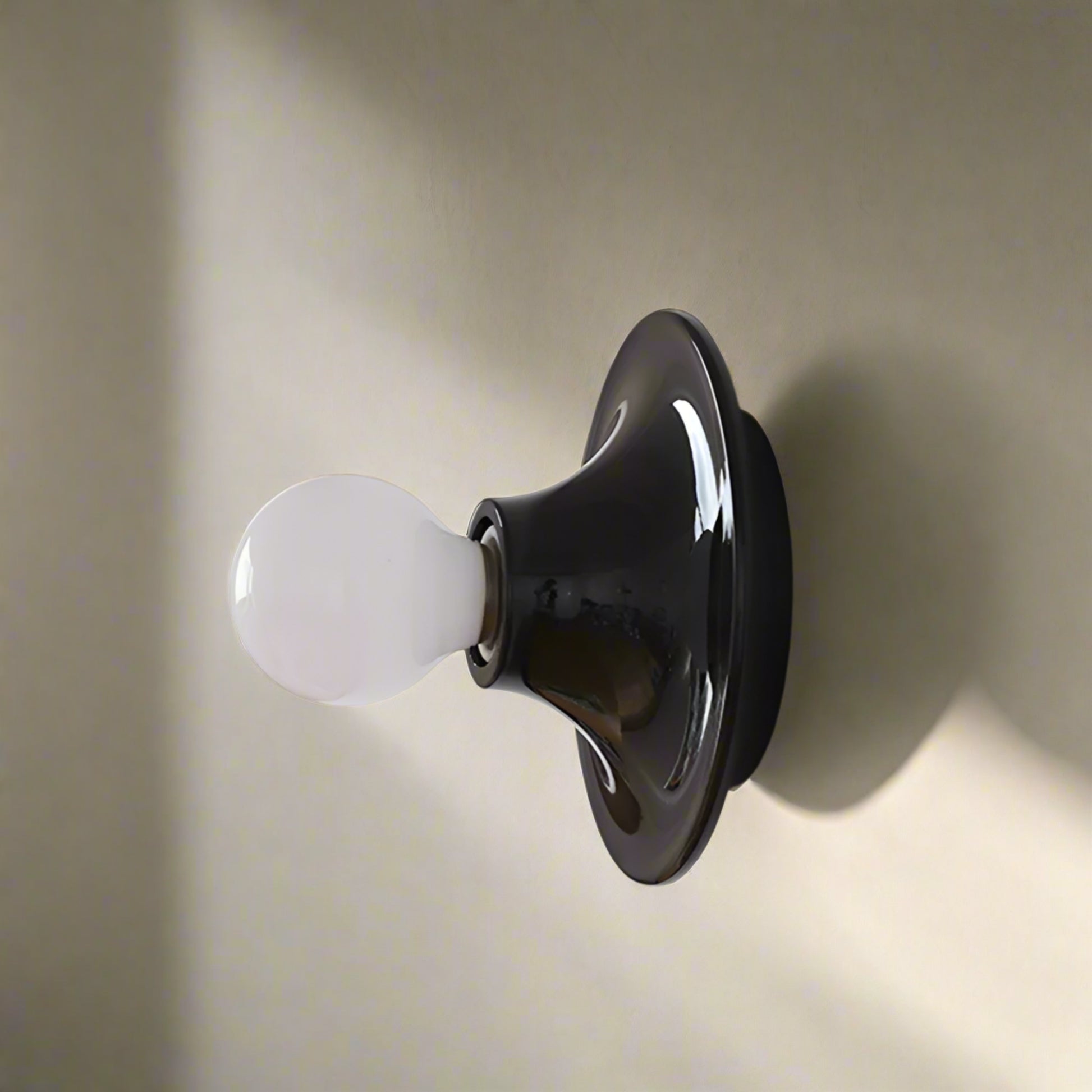 Black wall light fixture with a white bulb on a light gray background