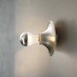 Chrome wall-mounted light fixture on a white wall with a plant in the corner.
