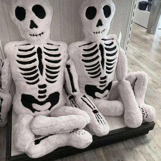 Two plush skeleton toys sitting on a wooden surface.