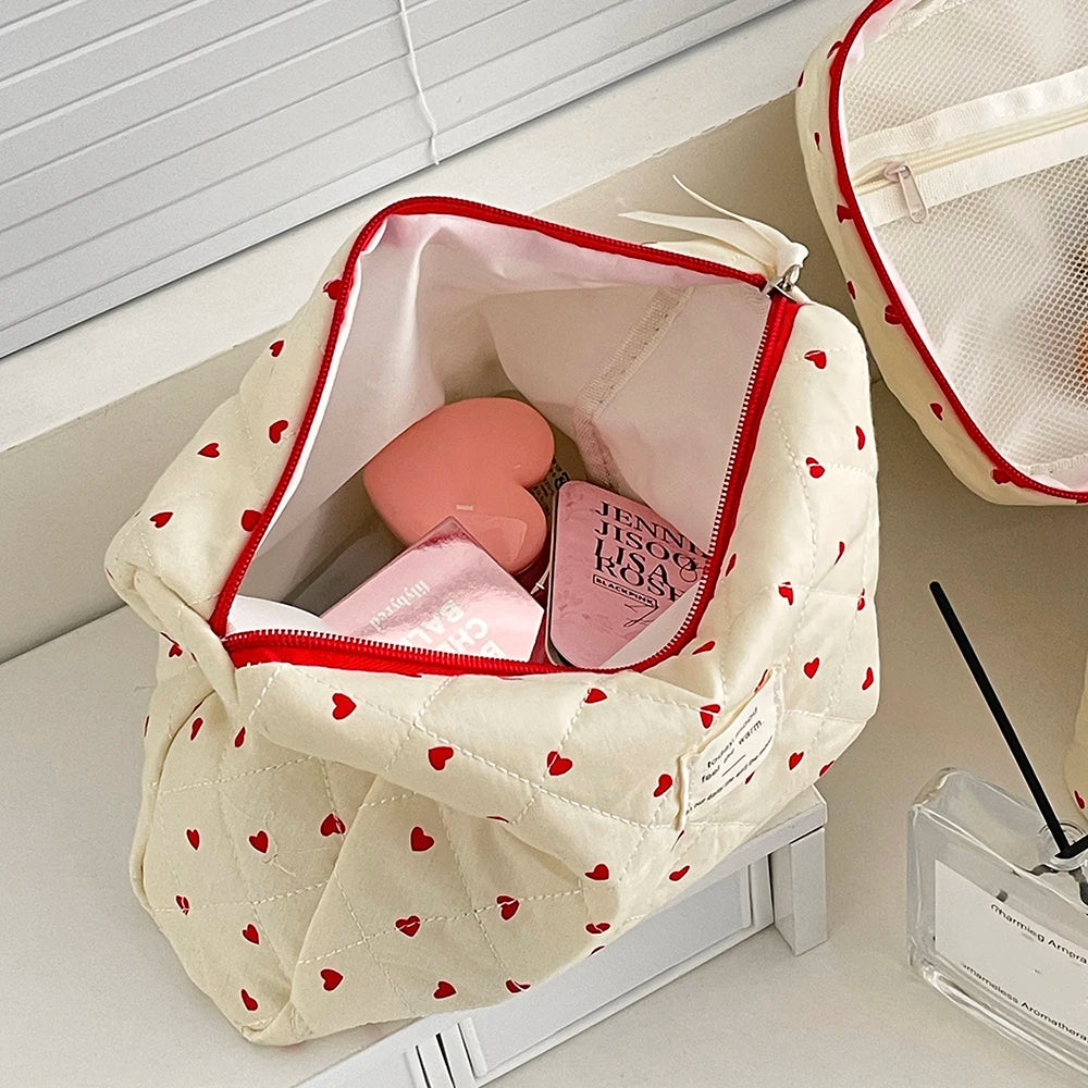Cosmetic bag with heart patterns containing beauty products on a white surface.