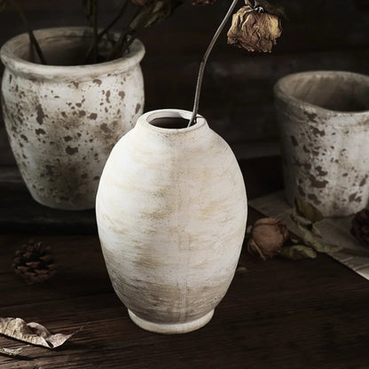 White ceramic vase on a dark surface with other ceramic pots in the background