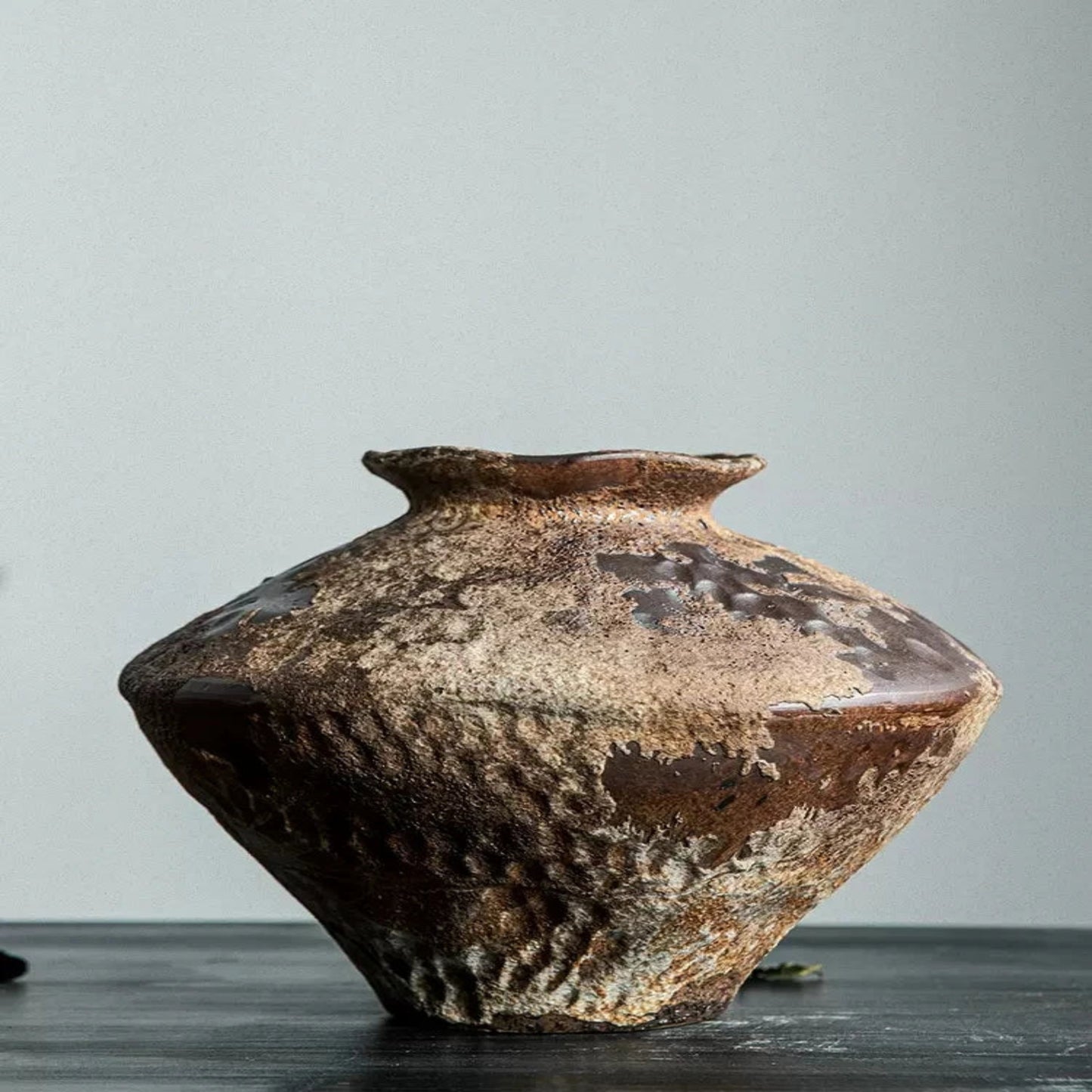 Rustic brown ceramic vase on a gray surface with a neutral background