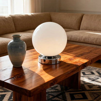 White spherical lamp and gray vase on a wooden coffee table with a beige sofa in the background.