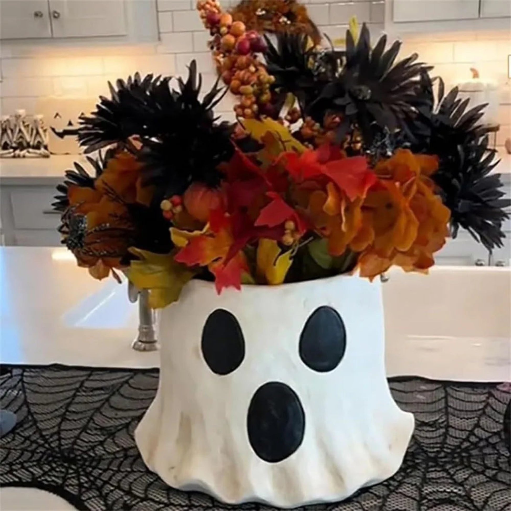 Halloween-themed ghost vase with autumn leaves on a kitchen counter.