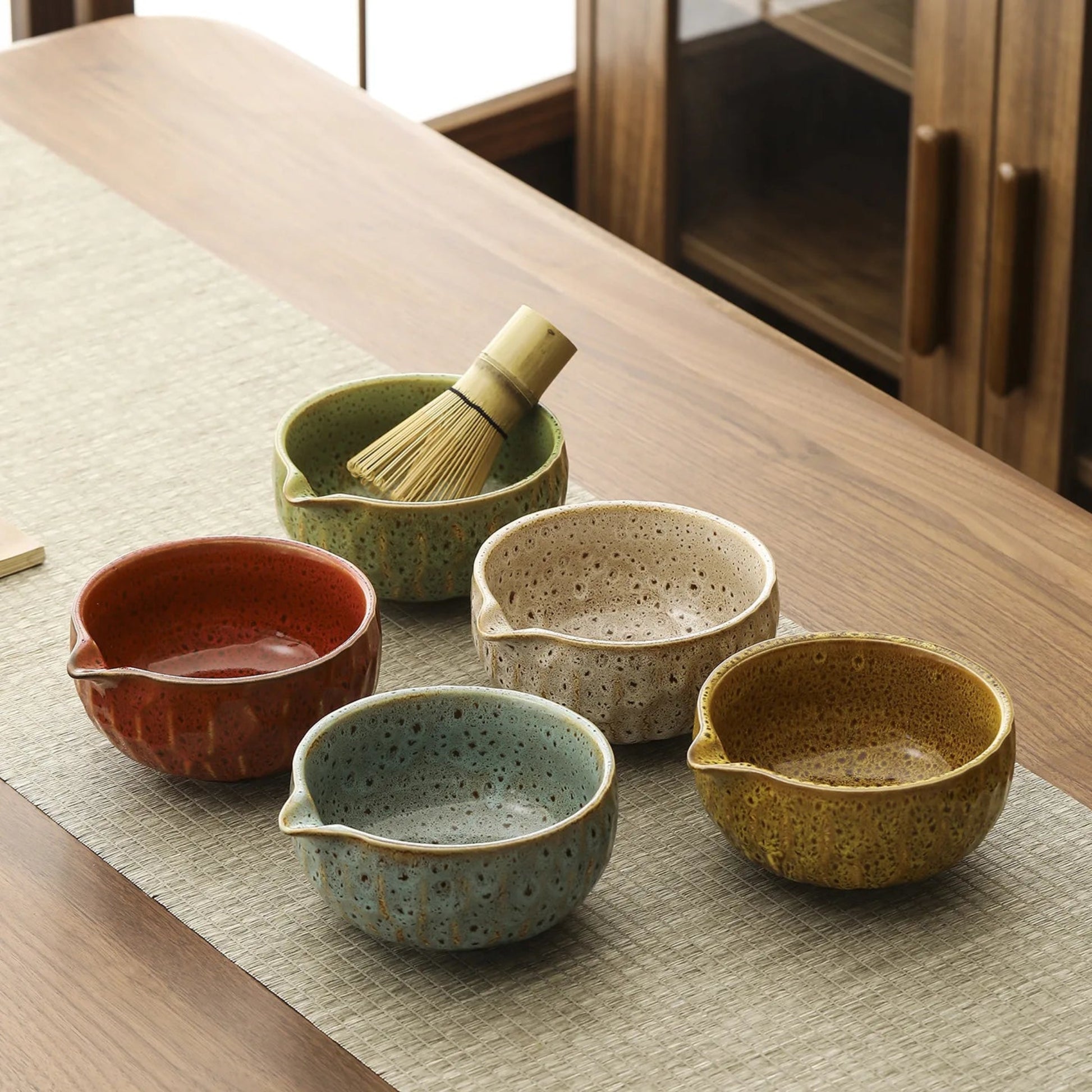 Set of ceramic bowls on a wooden table with a whisk.