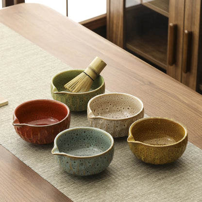 Set of ceramic bowls on a wooden table with a whisk.