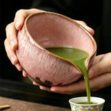 Ceramic bowl being filled with green tea into a smaller cup.
