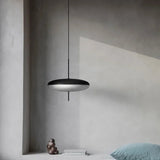 Modern black pendant light hanging in a minimalistic room with concrete walls and a blue pillow.