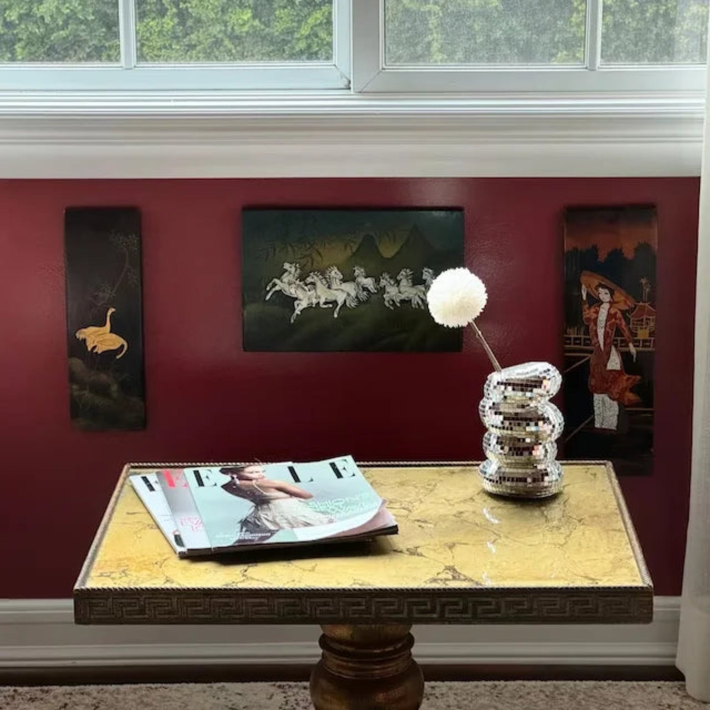 Decorative table with magazine and lamp against a red wall with framed pictures