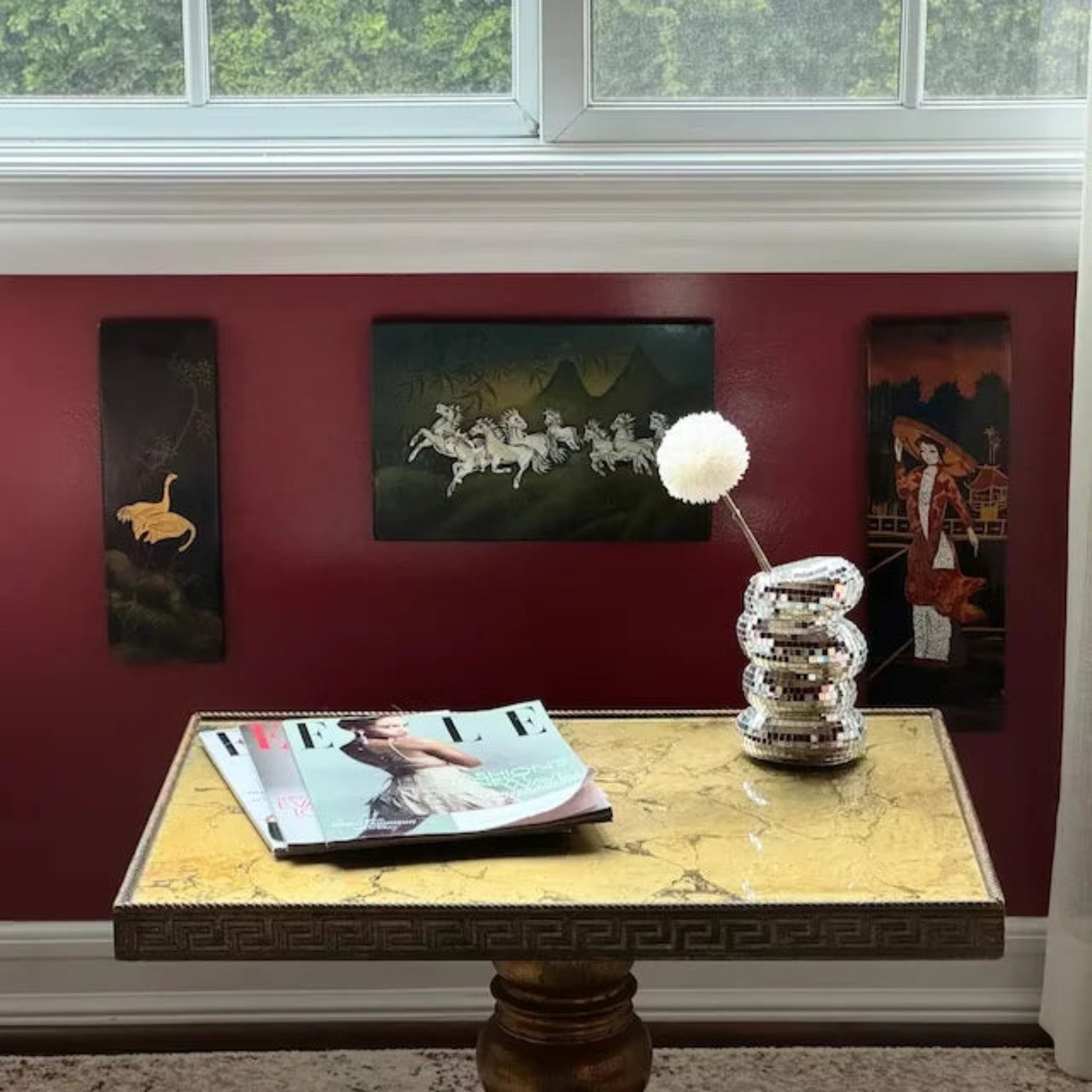 Decorative table with magazine and lamp against a red wall with framed pictures