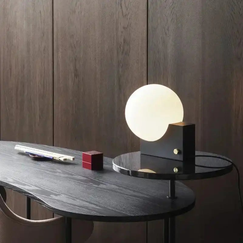 Stylish dimmable LED table lamp with glass globe and black base on a designer desk. Perfect for contemporary workspace decor.