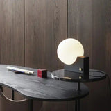 Stylish dimmable LED table lamp with glass globe and black base on a designer desk. Perfect for contemporary workspace decor.