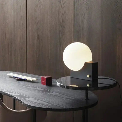 Stylish dimmable LED table lamp with glass globe and black base on a designer desk. Perfect for contemporary workspace decor.