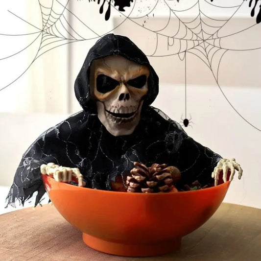 Skeleton figure in a black hooded outfit with a bowl of pine cones, Halloween-themed background.