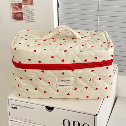 Quilted storage bag with red heart patterns and a red zipper on a white surface.