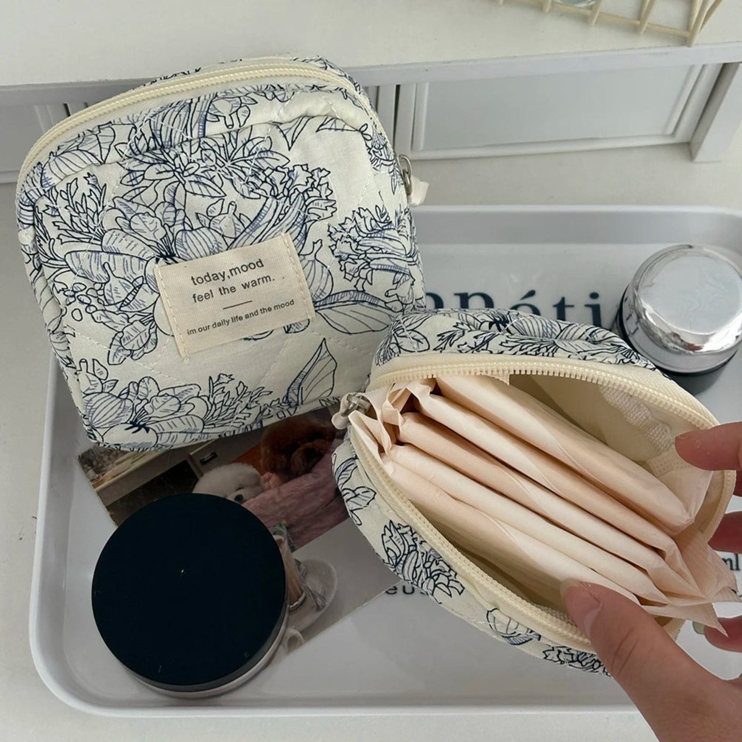 Floral-patterned cosmetic bag with a hand holding an open inner pouch on a white surface.