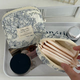 Floral-patterned cosmetic bag with a hand holding an open inner pouch on a white surface.