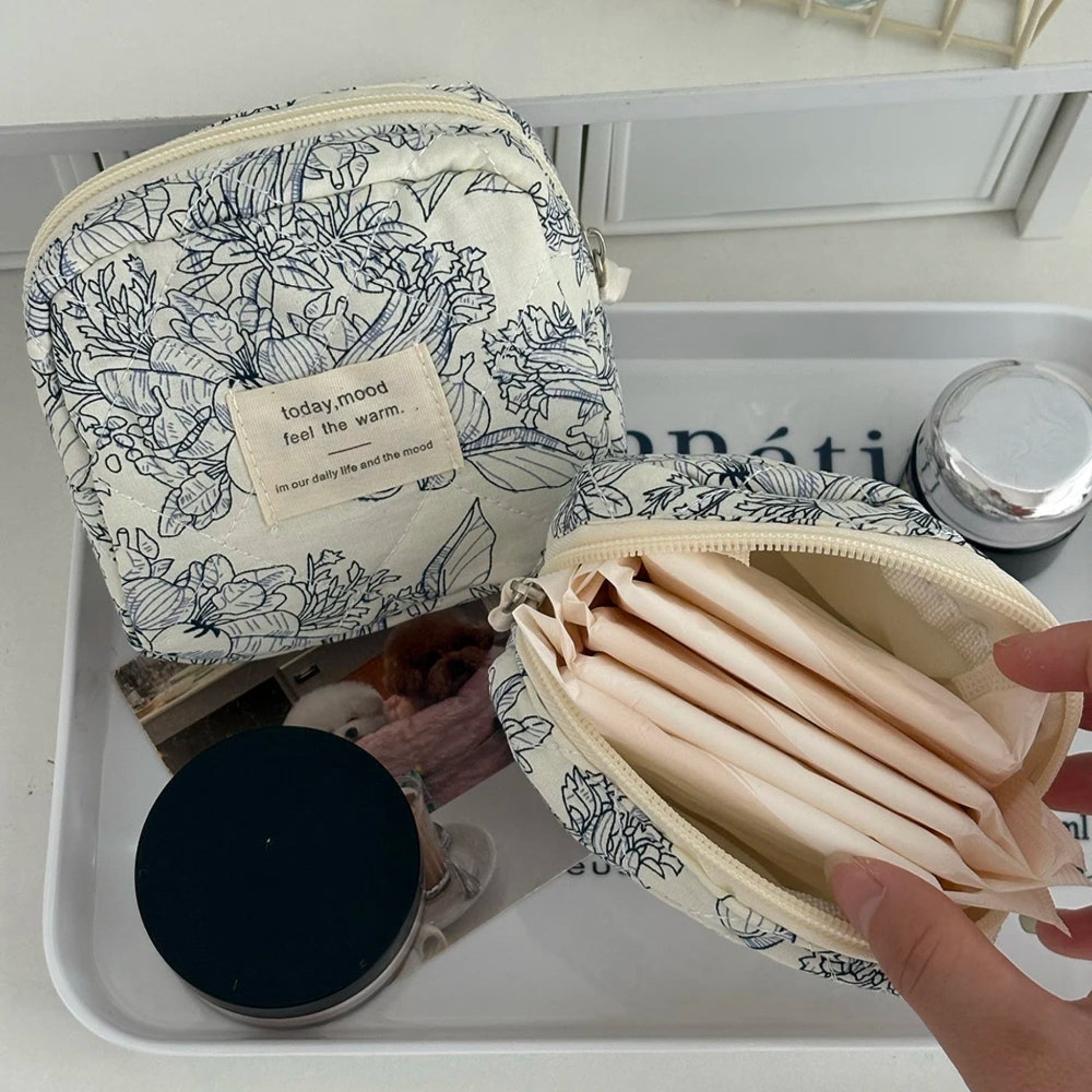Floral-patterned cosmetic bag with a hand holding an open inner pouch on a white surface.