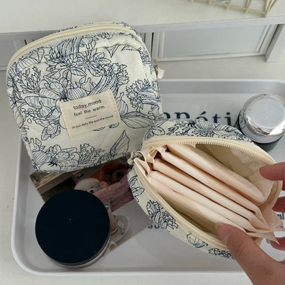 Floral-patterned cosmetic bag with a hand holding an open inner pouch on a white surface.