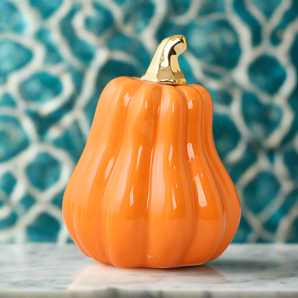 Orange ceramic pumpkin with a gold stem on a marble surface with a blurred background