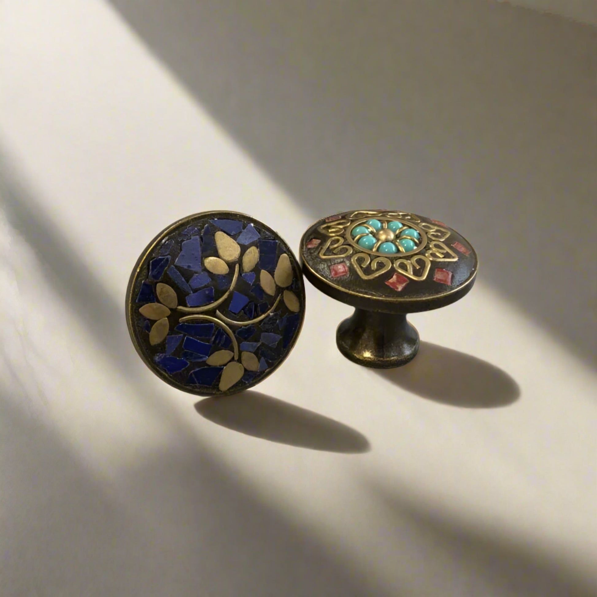 Two decorative cabinet knobs with intricate designs on a plain background