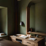 Wooden desk with books and a lamp in a dimly lit room with green walls.
