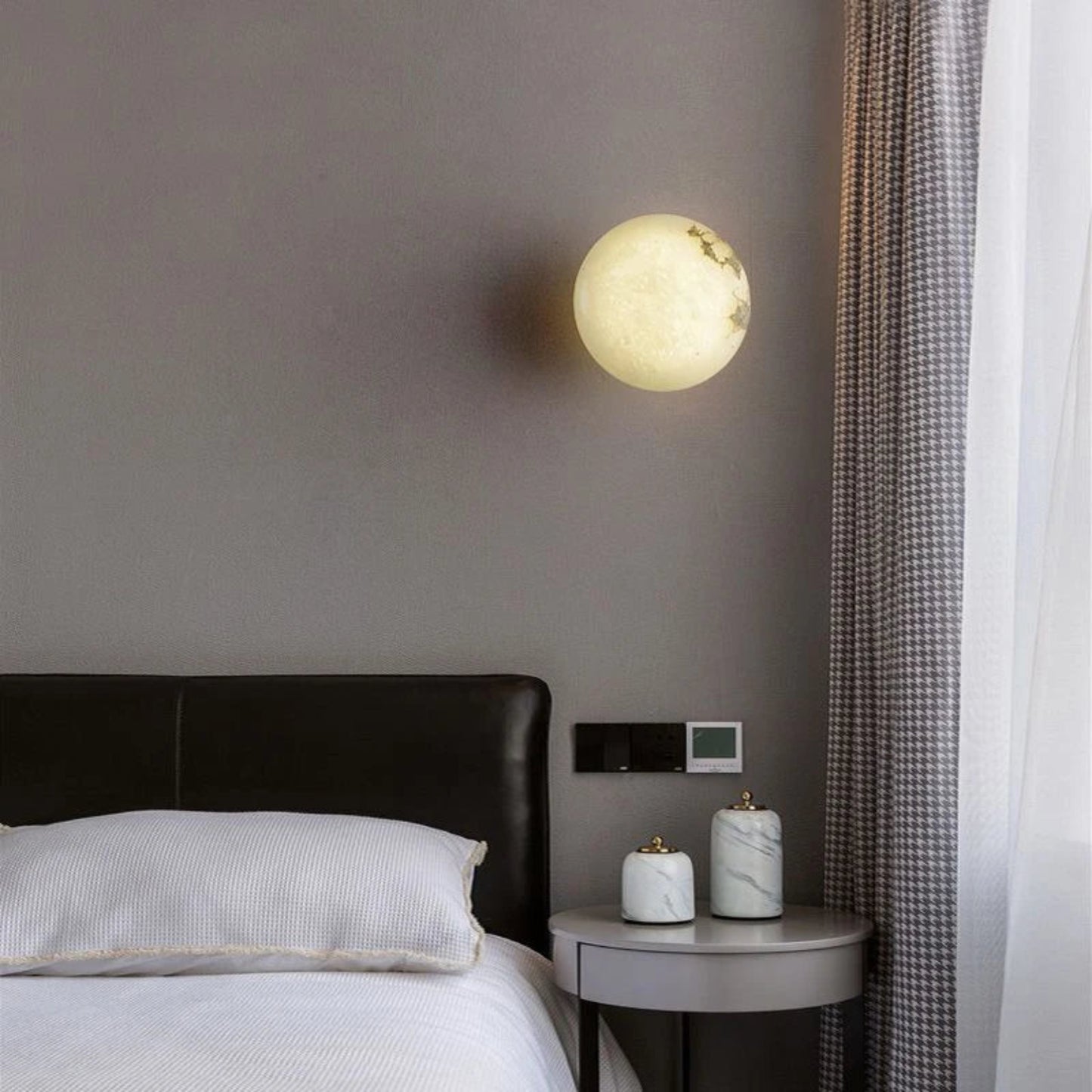 Modern bedroom with a round wall light fixture, bed, and side table.