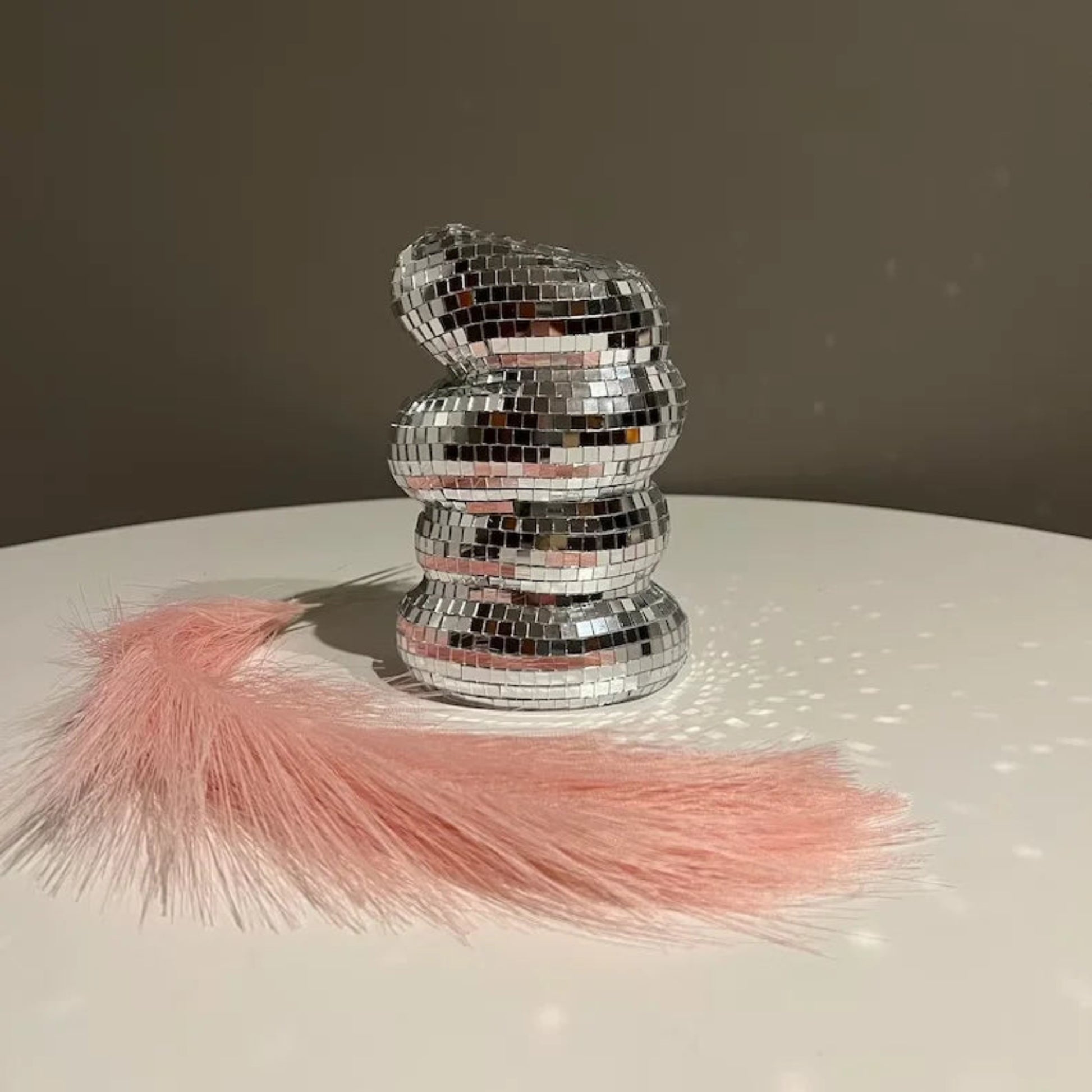 Stack of silver disco balls with pink tassels on a reflective surface