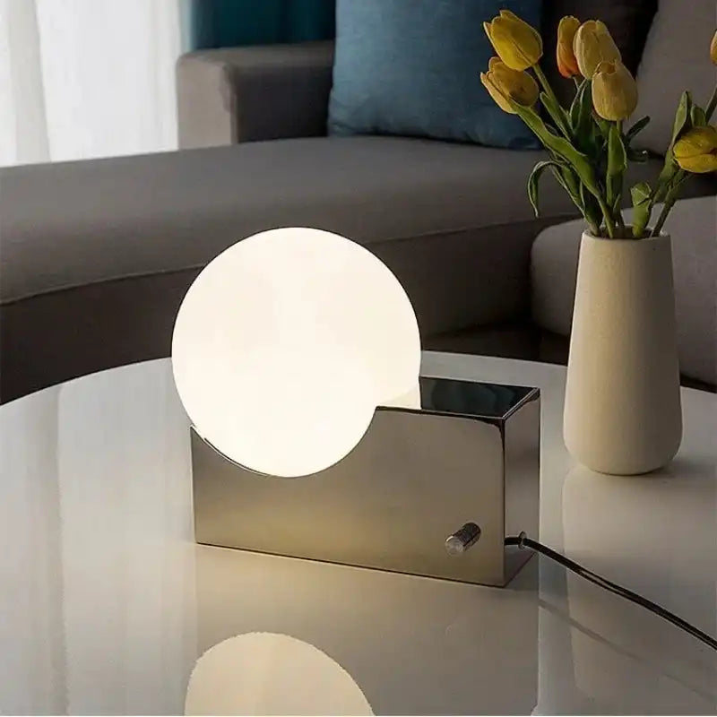 Decorative LED table lamp with dimmable glass globe and stainless steel base on a white coffee table. Ideal for living room lighting.
