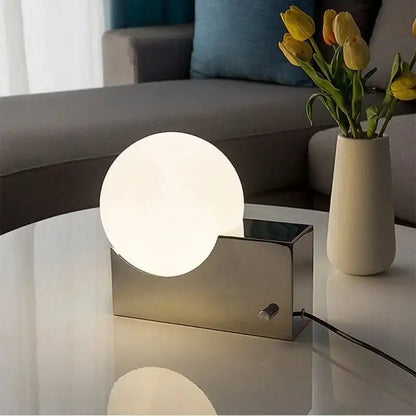 Decorative LED table lamp with dimmable glass globe and stainless steel base on a white coffee table. Ideal for living room lighting.