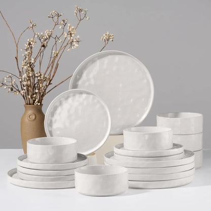 Set of white ceramic dinnerware with a vase of dried flowers on a gray background