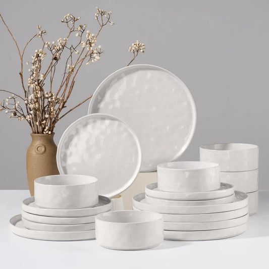 Set of white ceramic dinnerware with a vase of dried flowers on a gray background