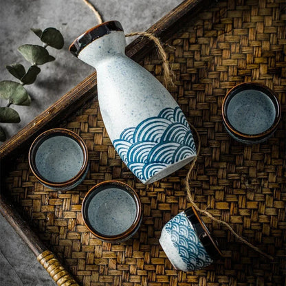 Ceramic bottle with wave pattern and matching cups on a woven mat