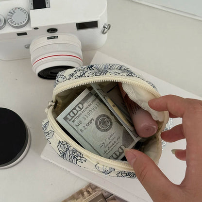 Hand holding a small pouch with money and a pink item, with a camera in the background.