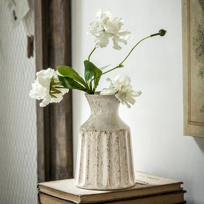 White flowers in a textured vase on top of books with a neutral background