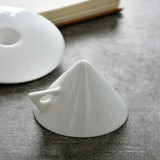 White ceramic funnel on a dark surface with a book in the background