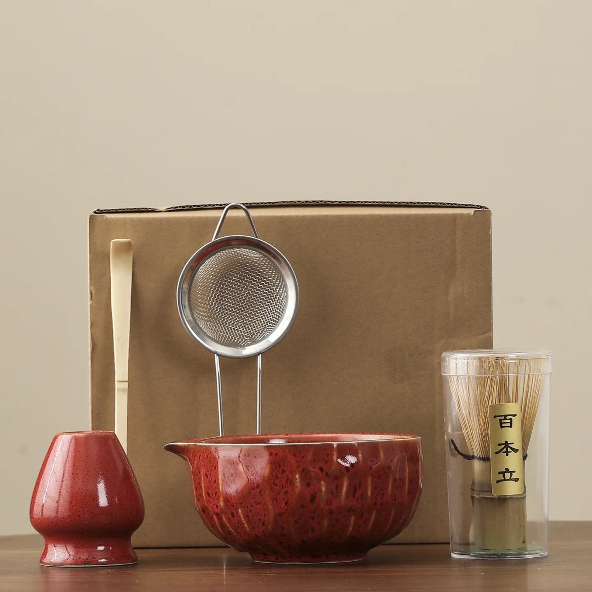 Tea-making set with a red teapot, strainer, and glass container on a beige background