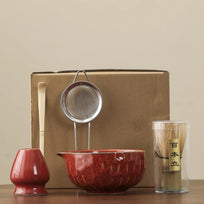 Tea-making set with a red teapot, strainer, and glass container on a beige background