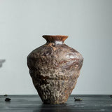 Textured ceramic vase on a dark surface with a light gray background