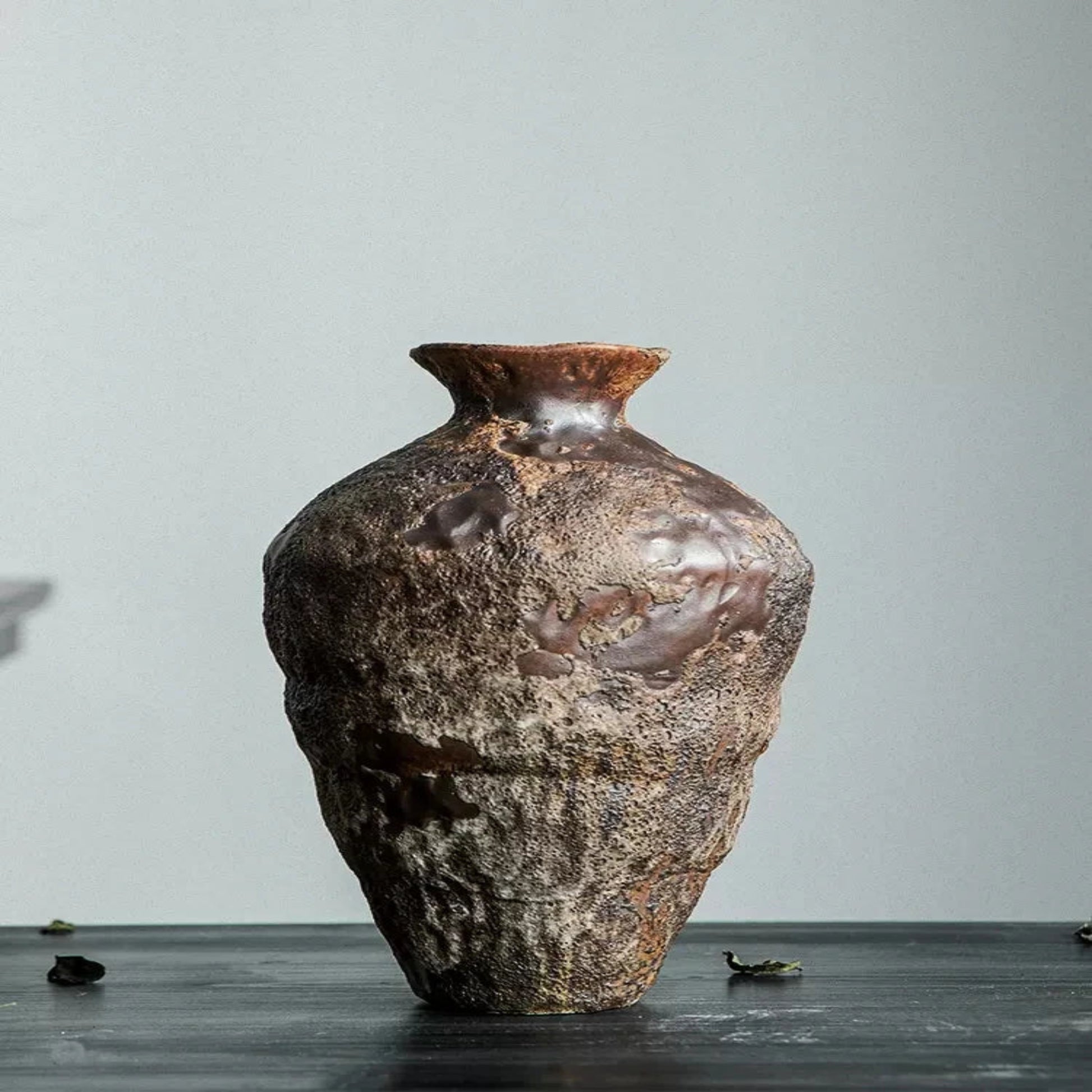 Textured ceramic vase on a dark surface with a light gray background