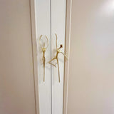 Gold door handles shaped like stylized figures on a white door.