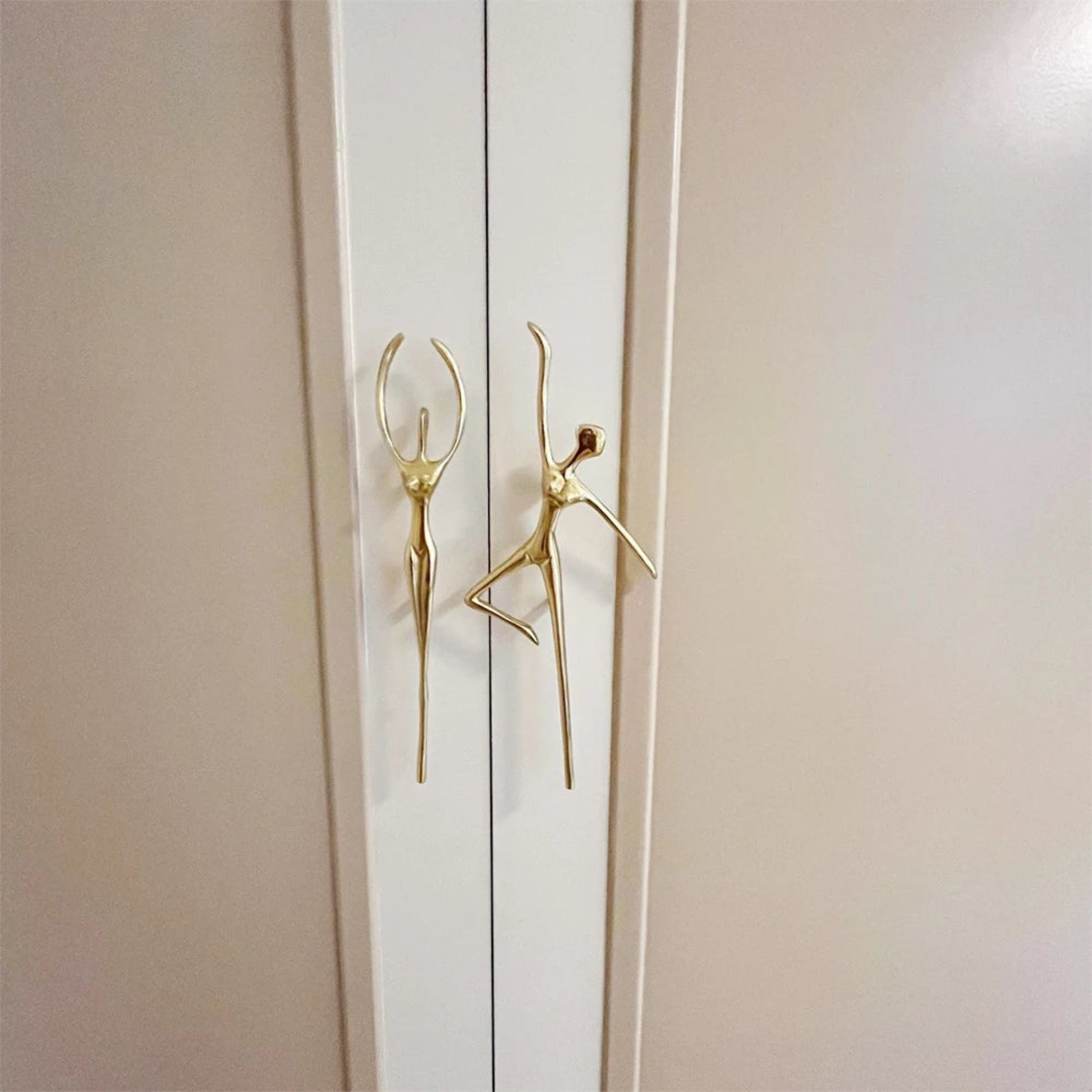 Gold door handles shaped like stylized figures on a white door.
