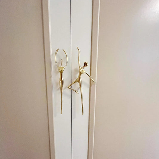 Gold door handles shaped like stylized figures on a white door.