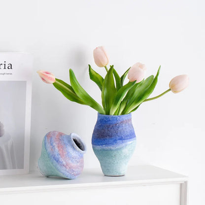 Two ceramic vases with a floral arrangement on a white surface.