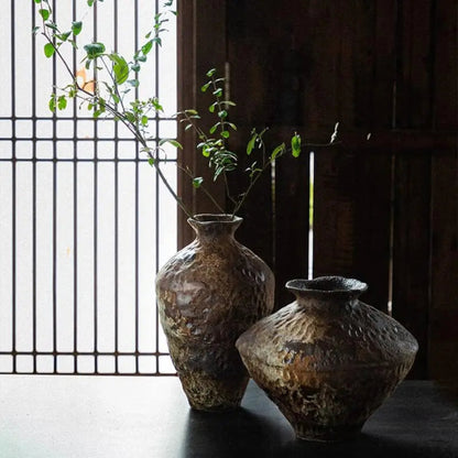 Two rustic vases with a plant against a wooden panel background