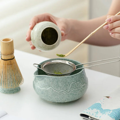 Tea-making process with a green ceramic bowl, whisk, and small container on a light surface.
